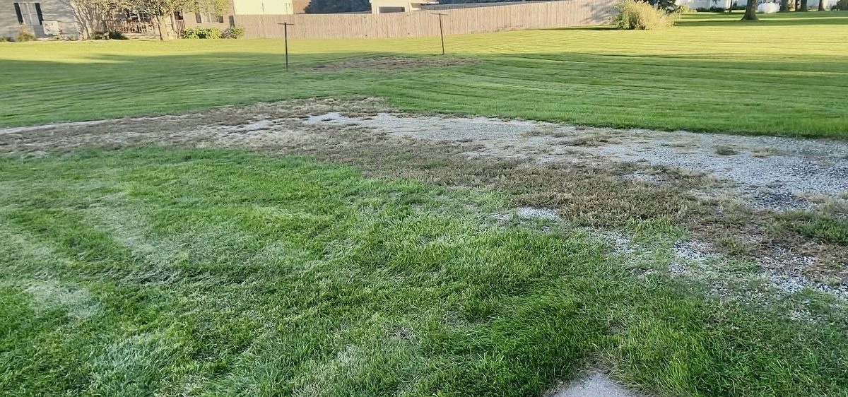 Weedy gravel area beside a garage before tractor work